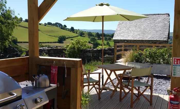 The BBQ and hob in Star's outdoor kitchen with a table and chairs under a parasol and a beautiful view of the hills in the background.